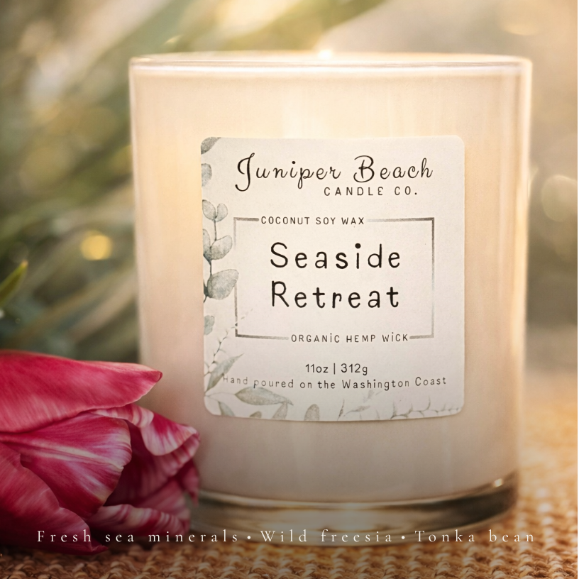Juniper Beach Candle Co. Seaside Retreat candle with a label on a textured surface with flowers.